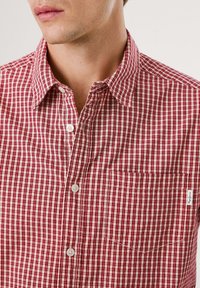 Rot-weiß kariertes Hemd mit Button-Down-Kragen, Taschen vorne und weißen Knöpfen, gefertigt aus weich strukturiertem Baumwollstoff.