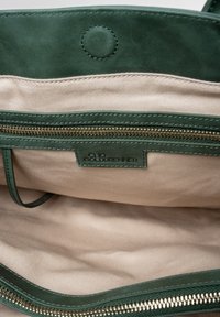 Groene leren tas interieur met een beige voering, voorzien van een ritszak en een logo-label. Glad textuur met contrasterende stiksels.