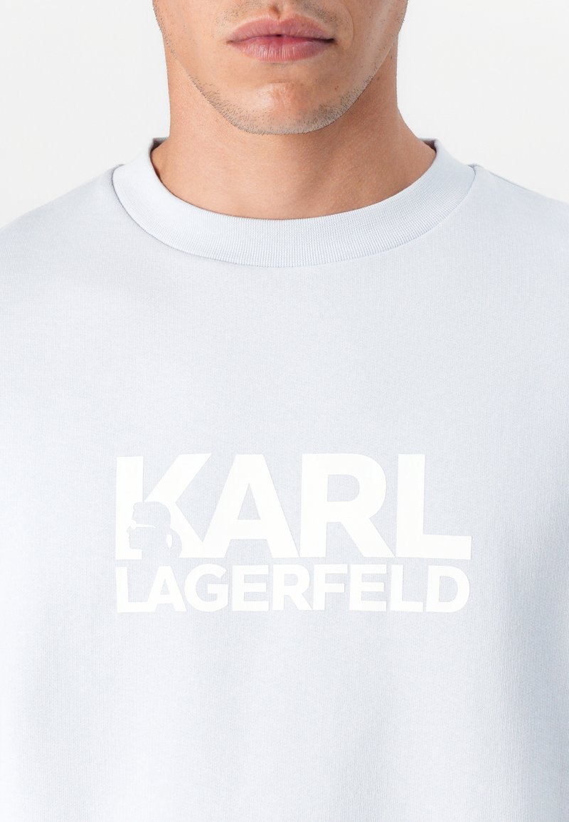 Sweat-shirt bleu clair avec un col rond, présentant un grand texte blanc "KARL LAGERFELD" et un logo en contour, fabriqué en tissu doux.