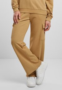 Khaki, weit geschnittene Cargo-Hosen aus einem weichen Baumwollmix mit Seitentaschen, kombiniert mit weißen Sneakern für einen lässigen Look.