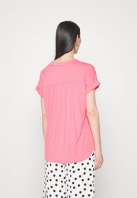 Rosa Kurzarm-T-Shirt mit rundem Ausschnitt und gerafftem Rückendetail, kombiniert mit schwarz-weißen gepunkteten Hosen. Weicher, leichter Stoff.