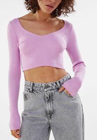 Pink ribbed crop sweater with long sleeves paired with high-waisted gray denim jeans. The texture is soft with a fitted silhouette.