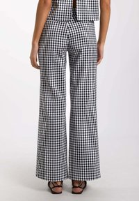 Pantalones de pierna ancha de cuadros vichy en blanco y negro con cintura alta; tela texturizada; combinados con sandalias negras de tiras; costuras visibles.