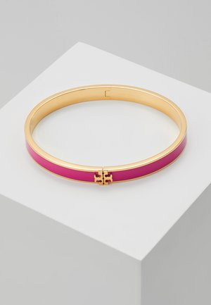 Gouden bangle armband met een glanzende diepproze emaille ingelegd en een kleine gouden logo sluiting, getoond op een wit platform.