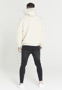 Flauschiger weißer Hoodie mit hohem Kragen und übergroßem Design, kombiniert mit schwarzen Skinny-Jeans und weißen Sneakern.