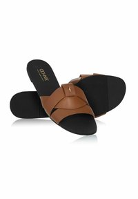 Brązowe skórzane sandały na suwak z krzyżującymi się paskami, czarna gumowa podeszwa i teksturowana wkładka. Złoty akcent z logo na górnym pasku.