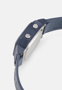 Sport watch with a matte navy silicone strap, silver stainless steel case, and two side buttons. Surface exhibits smooth texture.