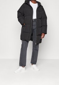 Black puffer coat with a quilted design, featuring a zip front and hood, paired with dark gray jeans and white sneakers.