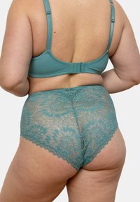 Un ensemble de bralette en dentelle turquoise et de culotte taille haute présentant des motifs floraux, une texture douce et des bords festonnés, vu de dos.