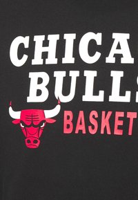Svart bomull t-shirt med fet vit text "CHICAGO BULLS" ovanför en röd tjur logotyp, med "BASKET" i rött under. Enkel design.