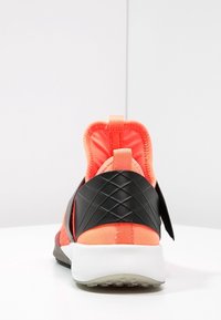 Scarpe sportive nere e corallo brillante con un tallone testurizzato e una tomaia liscia e stretch. Caratterizzate da un'etichetta per il tallone e suola bianca imbottita.