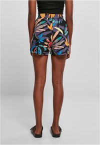 Shorts à imprimé floral avec un fond noir, une taille élastique et une longueur au-dessus du genou, associés à des sandales noires sans lacets.