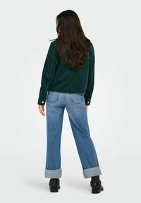 Zelená kordová blúzka s dlhým rukávom v kombinácii s bledomodrými riflami s vyhrnutými manžetami. Čierne členkové topánky dotvárajú outfit.