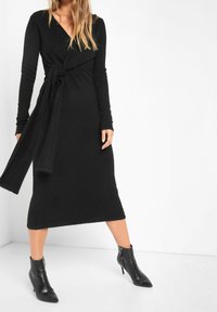 Czarna, długa sukienka kopertowa wykonana z miękkiego, teksturowanego materiału. Posiada związany w talii pas i midi długość, zestawiona z pointed ankle boots.