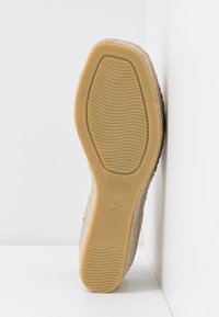 Semelle d'une chaussure espadrille beige avec semelle en caoutchouc, taille 37 marquée, fabriquée en Espagne, appuyée contre des murs blancs dans un coin.