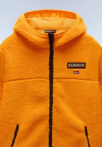 Fleecehuva jacka i klar orange med en strukturerad yta, med en frontdragkedja, bruna detaljer och en märkespatch.