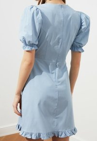 Helles blaues Kleid mit Puffärmeln, taillierter Brustpartie und ausgestelltem Saum mit Rüschensaum. Aus glattem Stoff mit einem sanften Glanz gefertigt.