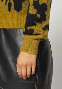 Hand rust op zwarte leren rok, met een mosterdgele en zwart gestreepte gebreide trui met geribbelde manchetten.