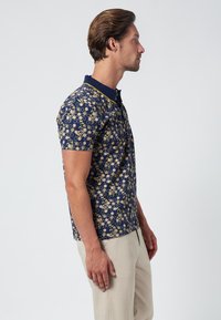 Korte mouwen polo in marineblauwe stof met een bloemmotief in gele tinten. Gestructureerd ontwerp met een contrasterende kraag en knopen.