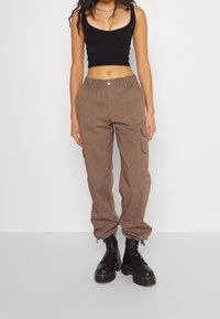 Brown cargo broek met een relaxte pasvorm, elastische tailleband en meerdere zijzakken, gecombineerd met een zwart nauwsluitend tanktop en zwarte veterschoenen.