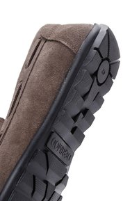 Zapato de ante marrón con una suela de goma negra texturizada que presenta un patrón de tacos para mayor tracción y un diseño de puntera suave y curvada.