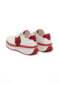 Sneaker bianche in pelle con accenti rossi, tallone rosso texturizzato, suola bianca spessa con motivo rigato e occhielli dorati visibili per i lacci.