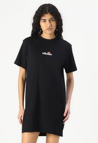 Juoda medvilnės t-marškinėlių suknelė su trumpomis rankovėmis. Su mažuoju baltu ir oranžiniu "ellesse" logotipu ant krūtinės. Lygi tekstūra ir laisvas kirpimas.