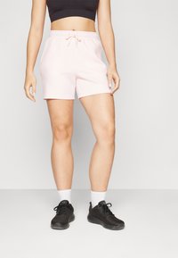 Bermudas de mezcla de algodón rosa con cintura elástica y cordón. Llevadas con zapatillas deportivas negras y calcetines blancos hasta el tobillo.
