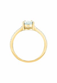 Anello in oro giallo con una pietra preziosa trasparente, rotonda e sfaccettata, incastonata in una montatura a griffe, e con pietre più piccole incastonate lungo la banda per un tocco di accento.