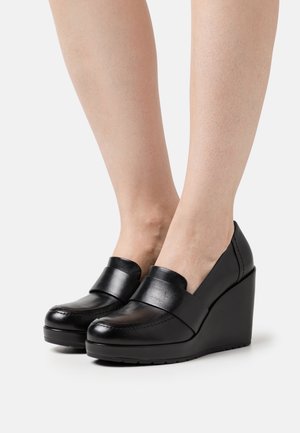 Schwarze Lederkeilabsätze mit runder Zehenform, die eine glatte Oberfläche und einen breiten Riemen an der Vorderseite aufweisen. Gummisohle für gute Traktion.