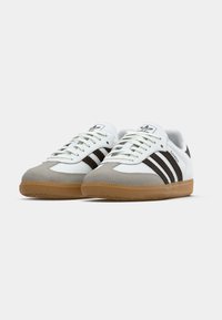 White and grey sneaker with three brown stripes. Features a suede toe, rubber gum outsole, and classic design elements.
