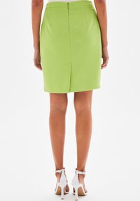 Grüne Bleistiftrock mit strukturierter Oberfläche, Reißverschluss hinten und Schlitz. Kombiniert mit weißen High-Heel-Sandalen. Glattes, figurbetontes Design.