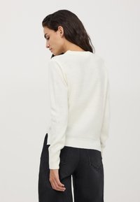 Maglione a maglia color crema con maniche lunghe, tessuto testurizzato, polsini e orlo a coste, dotato di scollatura rotonda e vestibilità morbida.