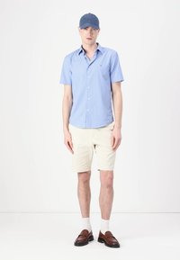 Lyseblå stribet kortærmet skjorte, beige shorts, hvide sokker og brune loafers. En blå kasket fuldender outfittet.