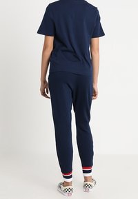 Námořnická modrá bavlněná tričko spárované s odpovídajícími joggery s pruhovanými akcenty na manžetách. Oblečení má uvolněný, ležérní střih.