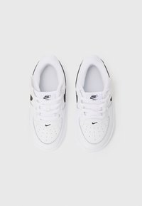Sneakers brancos em couro com detalhes pretos, biqueira perfurada, atacadores planos e a marca Nike na língua e no lado. Sola em borracha.