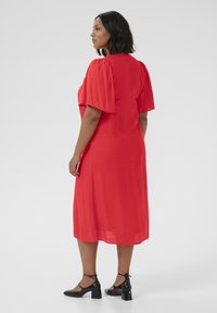 Abito midi rosso con maniche corte a palloncino e una vestibilità rilassata. Indossato con scarpe con tacco nere, che mettono in risalto una trama del tessuto liscia e leggera.