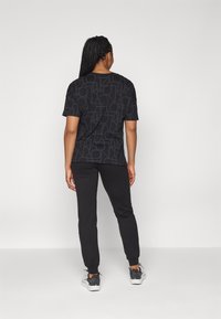 Must t-särk geomeetrilise mustriga, kombineeritud mustade joggeritega. Komplekt on lõdva lõikega ja pükstel on soonikkoes varrukad.