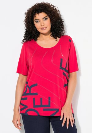 T-shirt rouge à manches courtes, avec un col rond, présentant des accents de texte bleu foncé dans un motif diagonal et des détails métalliques pour la texture.
