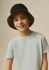 Zwarte bucket hat met een grijze rand, gedragen met een lichtgrijze katoenen t-shirt. De stof heeft een zachte textuur en het shirt heeft een ronde hals.