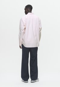 Cămașă roz deschis cu dungi, cu nasturi, mâneci lungi, croială lejeră, asortată cu pantaloni largi negri și adidași gri.