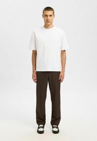 Witte katoenen t-shirt, relaxed fit, korte mouwen, gecombineerd met bruine broeken en zwarte schoenen met witte accenten. Eenvoudig en minimalistisch ontwerp.