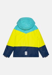 Gyerekdzseki kapucnival kék, sárga és teal színblokkokban, hátulról mutatva, hosszú ujjakkal és egy kis fehér folttal az alján.