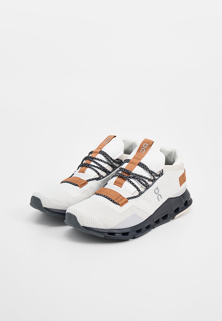 Weiße Sport Schuhe mit schwarzen Sohlen, braunen Ziehschlaufen und schwarz-weißen Schnürsenkeln, nebeneinander auf einem weißen Hintergrund platziert.
