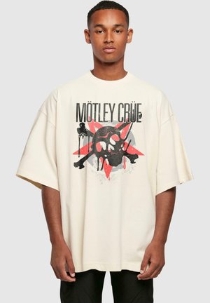 Creme oversized t-shirt med et grafik af skull og korslagte knogler med røde accenter på en stjerne-eksplosion baggrund. Korte ærmer, afslappet pasform.