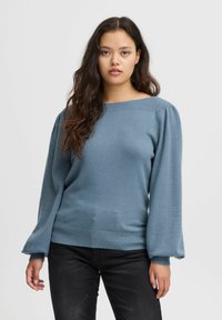 Pull bleu clair avec un col large, des manches bouffantes et des bords côtelés, fabriqué à partir d'un matériau tricoté doux.