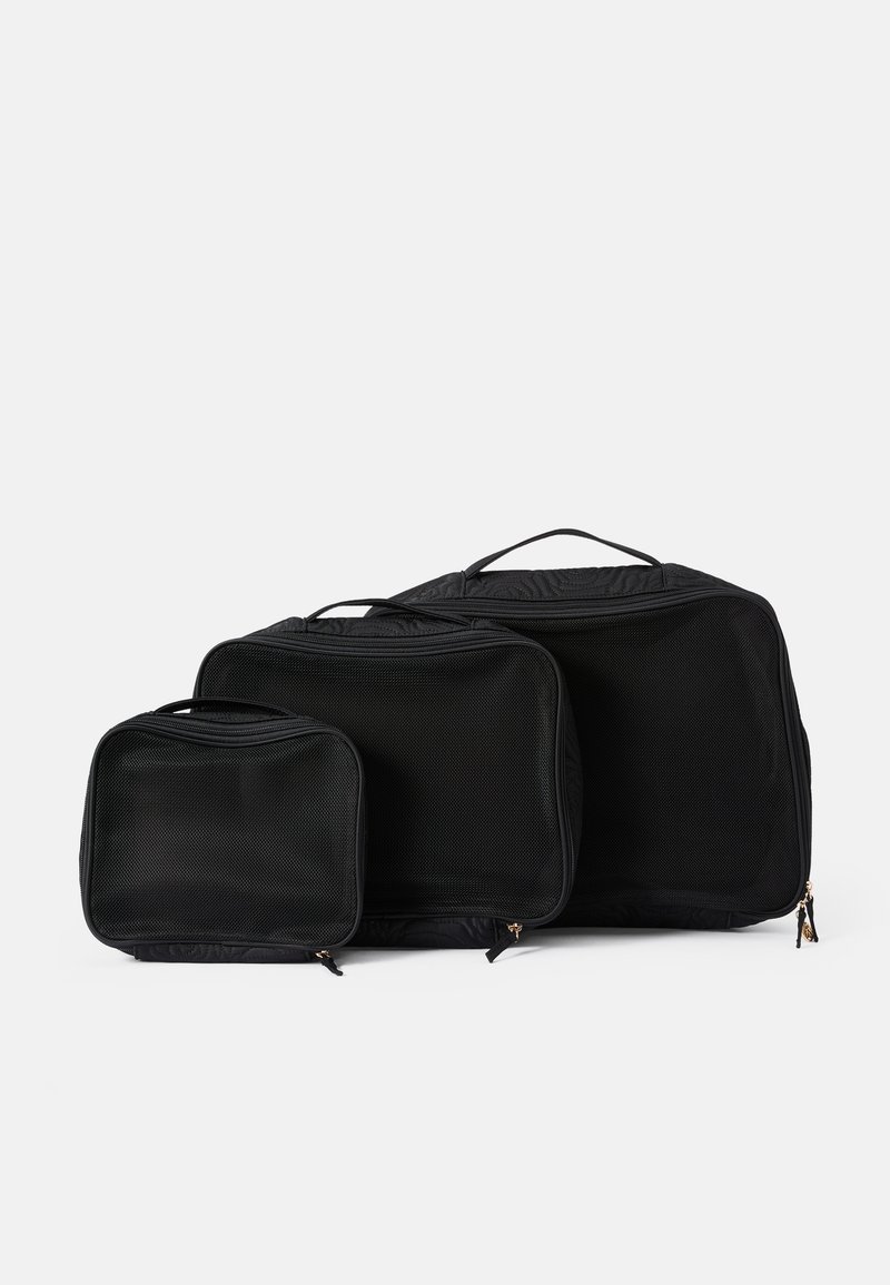 Trois organisateurs de voyage en maille noire de tailles variées, dotés de fermetures éclair et de poignées supérieures pour un transport facile. Surface texturée.