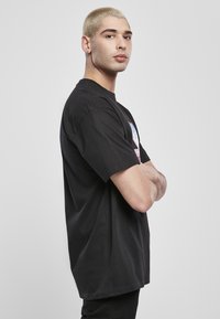 Fekete pamut póló rövid ujjakkal, laza szabással, az elején színes mintázattal és grafikával, oldalról nézve.