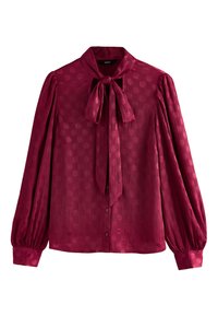 Blusa bordeaux con maniche lunghe a sbuffo, colletto con fiocco e motivo a pois in rilievo. Presenta bottoni frontali e polsini arricciati.