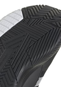Semelle de chaussure en caoutchouc noir avec des motifs de grip texturés. Présente une pièce d'accent blanche et un design de semelle varié pour une meilleure adhérence. Durable et flexible.